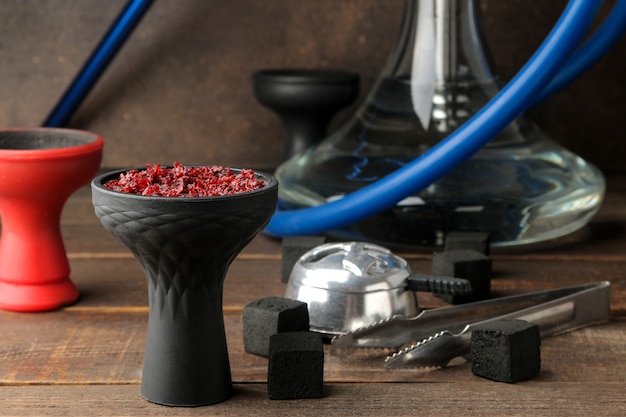 Silicone bowl for hookah with tobacco and various accessories for making hookah. coals, tongs, kolaud on a brown wooden table. close-up. accessories for hookah.