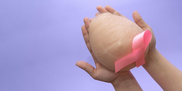 Silicone Breast Prosthesis On Woman Hands And Pink Ribbon. Breast Cancer Concept. Copy Space