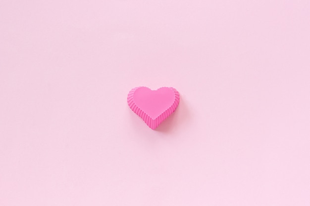 Silicone heart shaped mold dish for baking cupcakes on pink paper background.