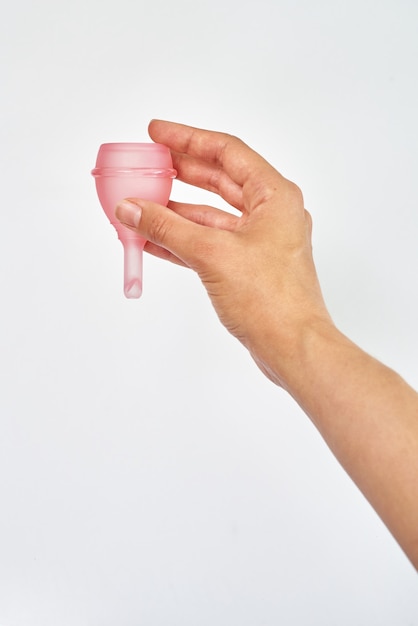 Silicone pink menstrual cup in female hand on white background