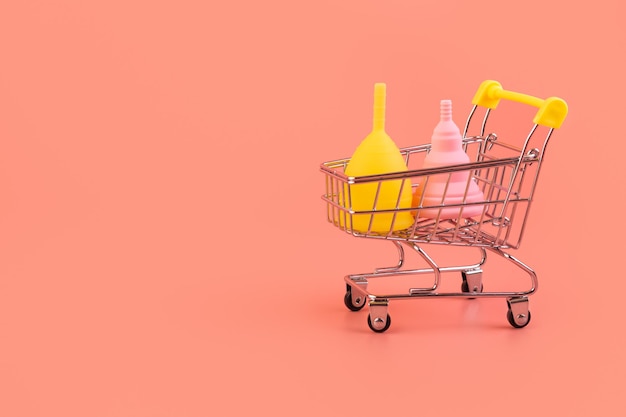 Silicone pink and yellow menstrual cup in shopping cart on pink\
background ecofriendly