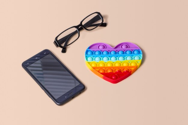 Photo silicone rainbow heart antistress pop it on a background with glasses and a phone.