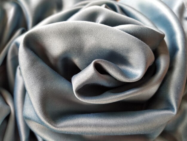 silky to the touch fabric of gray  blue color with a brilliant shimmer natural lighting light and shadow the material is casually folded into a circle resembling a rose bud polyester textile