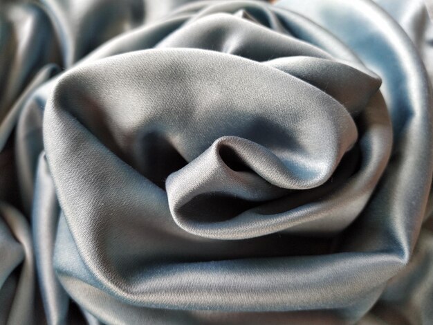 Silky to the touch fabric of gray  blue color with a brilliant shimmer Natural lighting light and shadow The material is casually folded into a circle resembling a rose bud Polyester Textile