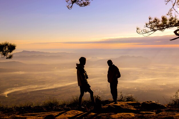 silluate tow man raise hand up and standing during sunset on top of mountain