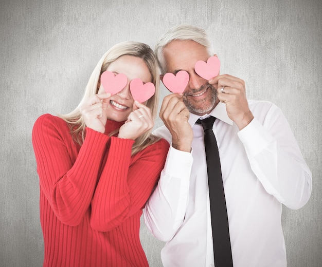 Photo silly couple holding hearts over their eyes against weathered surface