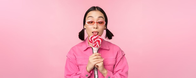 Silly and cute asian female model licking lolipop eating candy sweet and smiling looking excited sta