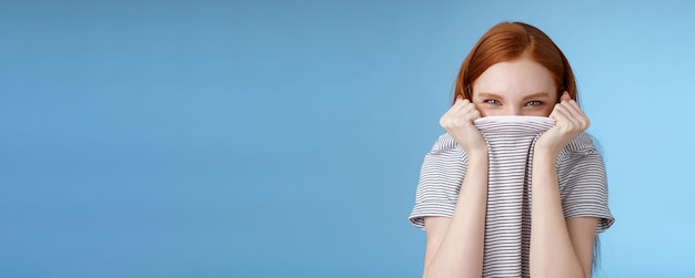 Silly flirty amused attractive playful redhead girlfriend hiding face pulling tshirt head squinting