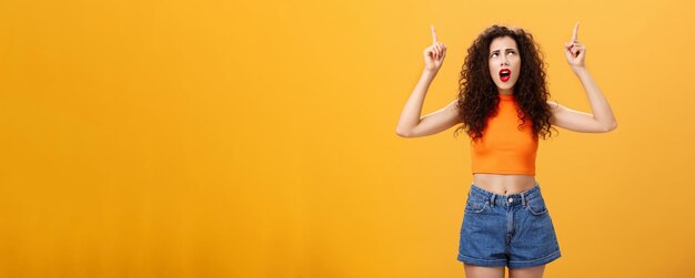 Silly and moody european party girl with curly hairstyle in red lipstic and stylish orange cropped t