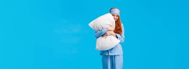 silly romantic and cute gentle young redhead coquettish woman in pyjama and sleep mask hugging pillo