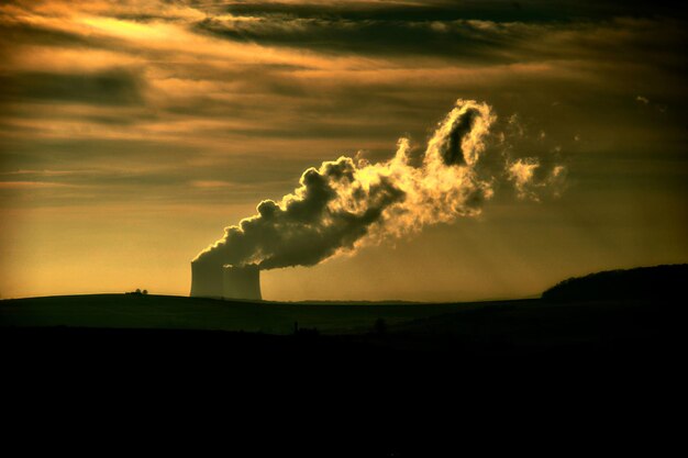 Foto silos che emettono fumo sul campo di silhouette contro il cielo durante il tramonto