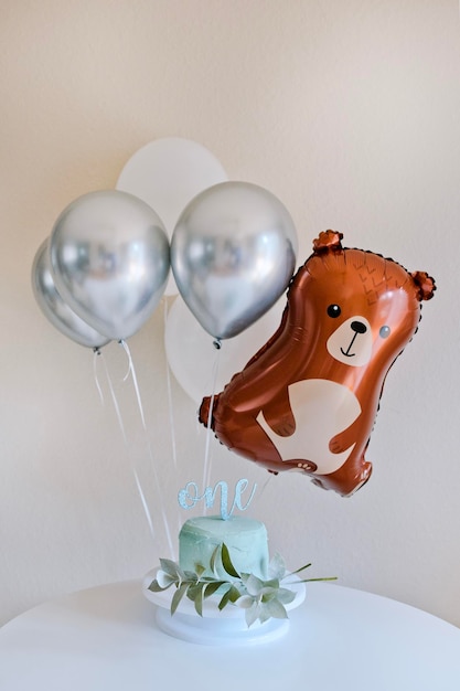 A silver balloon with a bear on it and small blue cake for first birthday cake smash