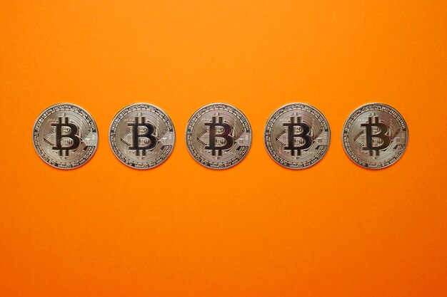 A silver bitcoin coins in horizontal row on orange wall. cryptocurrency