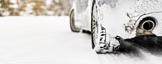 雪に覆われた道路に駐車した氷で覆われた銀色の車、後ろから排気する詳細ビュー、ぼやけた木の背景にテキストの左側の空きスペース