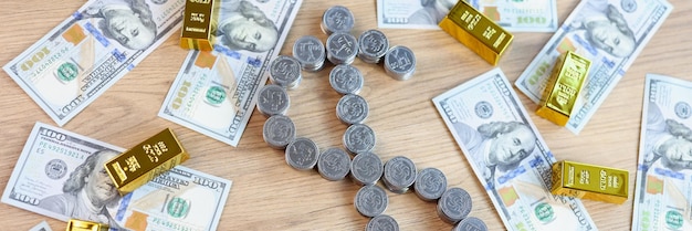 Silver coins in shape of dollar symbol and gold bars with dollar banknotes on wooden table