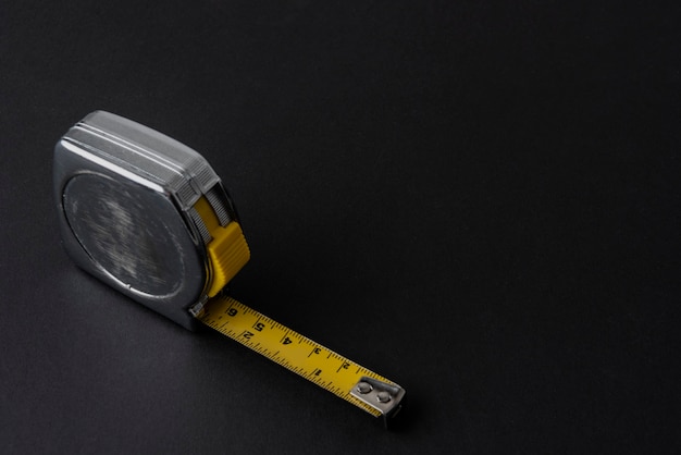 Silver colored flexometer or meter with yellow tape measure on a black background