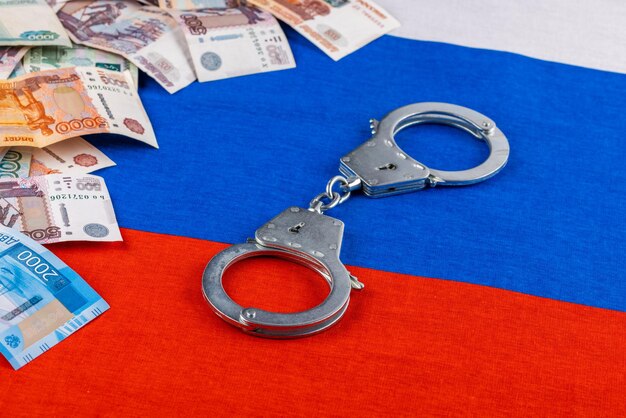 Photo silver colored handcuffs and russian paper rubles currency on russian flag background