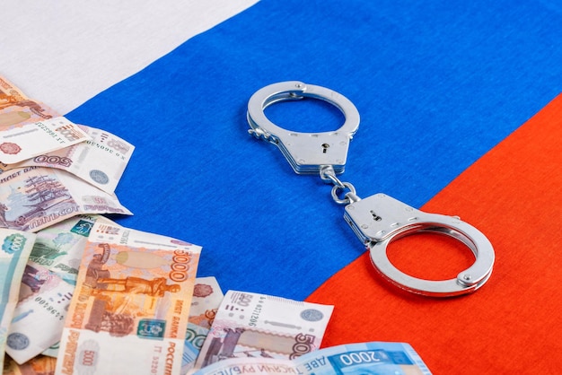 Silver colored handcuffs and russian paper rubles currency on russian flag background