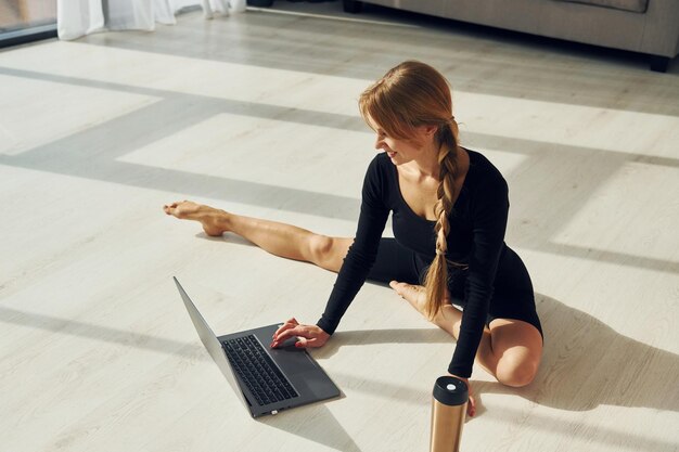 Silver colored laptop woman in sportive clothes doing yoga
indoors