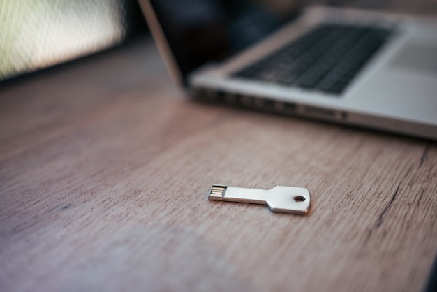 Silver colored USB-stick shaped like a key on a wooden table near the laptop.