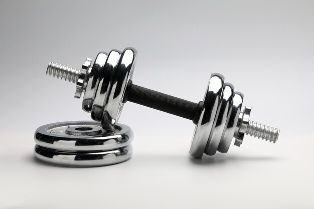 Silver coloured shiny metal dumbbell standing at pile of disks