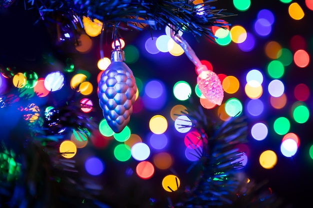 Cono d'argento palla di natale appesa a un albero di natale sullo sfondo molte ghirlande incandescente in diversi colori.