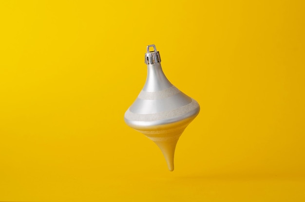 Silver cone shaped christmas ball floating in the air over bright yellow background