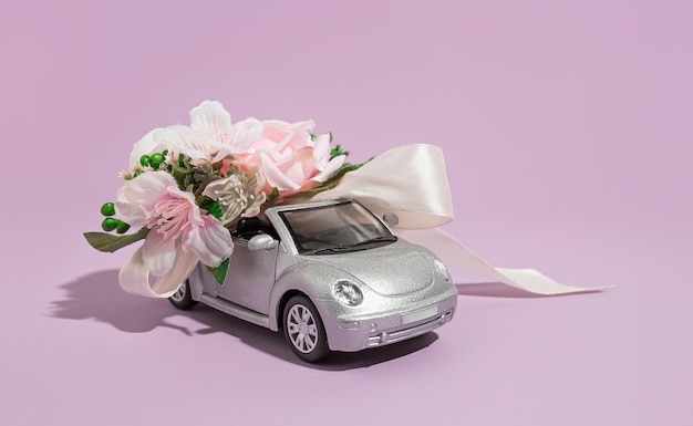 Silver convertible small car model with flowers on a purple background The concept of delivery