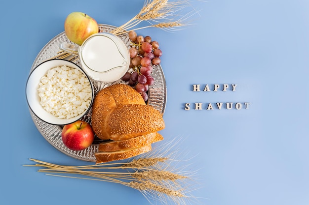 Серебряное блюдо с традиционными угощениями к весеннему празднику Шавуот, вид сверху на синем фоне с буквами счастливый шавуот