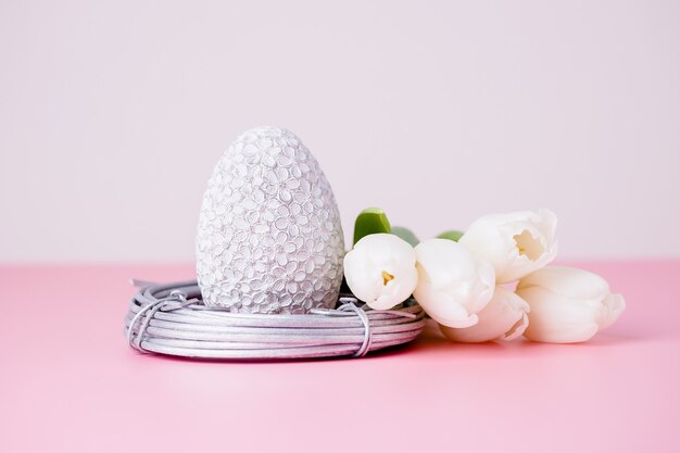 Silver easter egg in the nest and white tulips on a pink