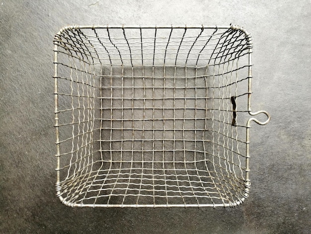 Photo silver empty wire basket with a square grid structure on a gray concrete floor in the kitchen