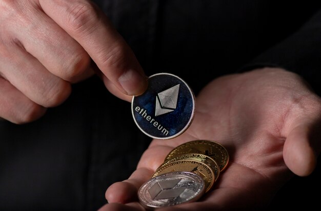 Silver ethereum coin of cryptocurrency in male hand palm over black background, close up. Eth putting into crypto pile.