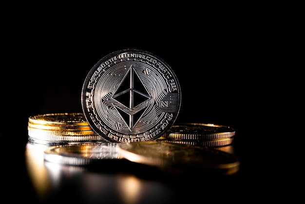 Silver Ethereum coin with other physical metal coins on black background