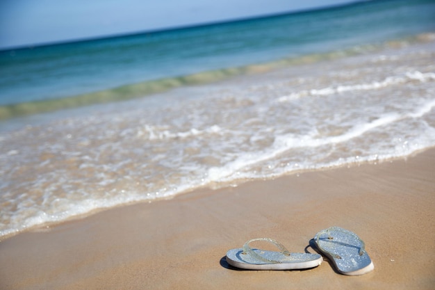 Silver flip flops on a sandy beach near a wave