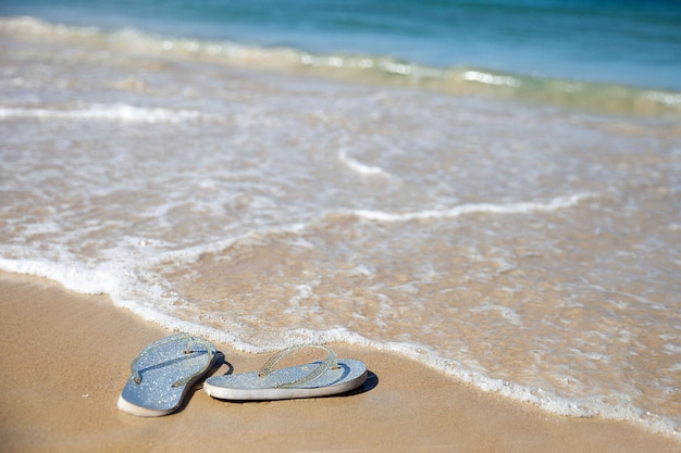 Silver flip flops on a sandy beach near a wave