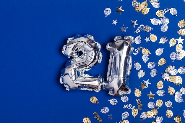 Silver foil number 21 balloon on a blue background with glitter gonfetti