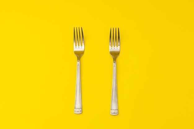 Silver forks lie on a yellow background minimalism