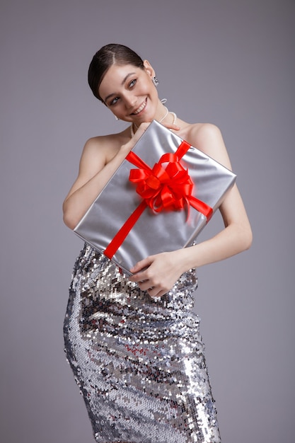 Silver Gift Box red bow Elegant woman in sequin dress on gray background Gathered dark hair