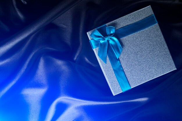 Silver gift box with blue bow background black silk fabric