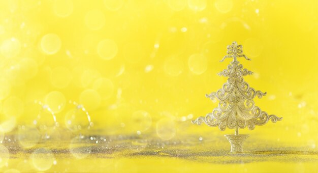 Silver glitter Christmas tree on yellow background with lights bokeh, copy space. 