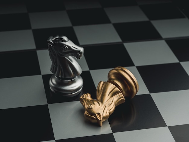 The silver horses, knight chess piece standing near the loser golden chess piece who fallen on chessboard background. Leadership, winner, loser, competition, and business strategy concept.