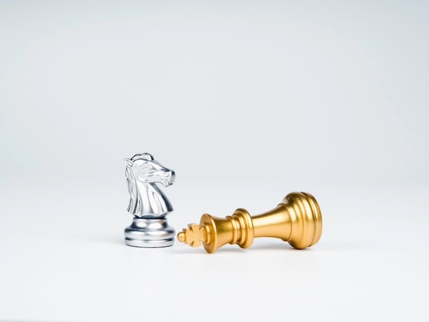 The silver horses knight chess piece standing near the loser golden king chess piece who fell isolated on white background Leadership winner loser competition and business strategy concept