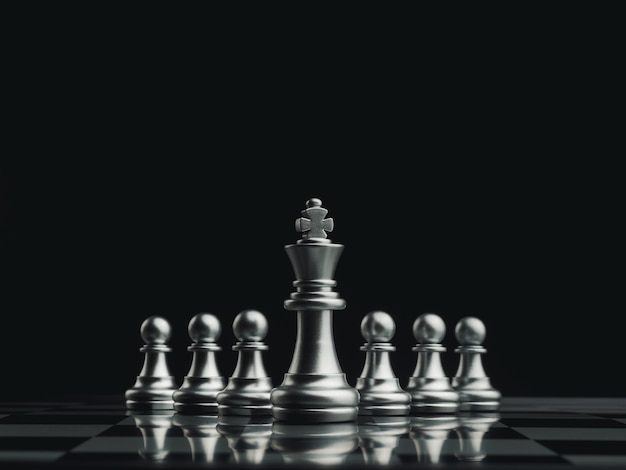 The silver king chess piece standing in front of pawn chess pieces on chessboard on dark background. Leadership, follower, team, commander, competition, and business strategy concept.