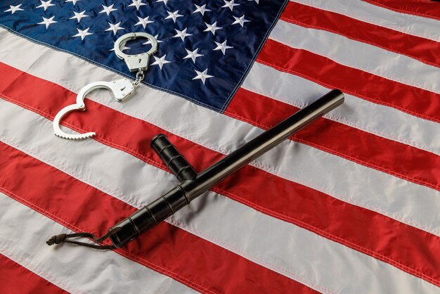 Photo silver metal handcuffs and police nightstick over us flag on flat surface