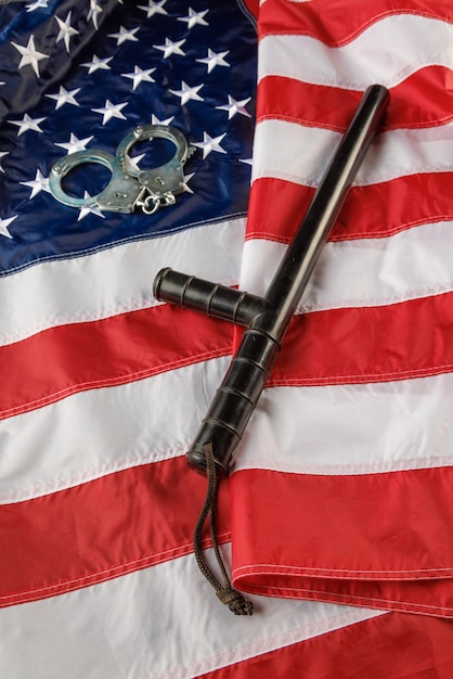 Серебряные металлические наручники и полицейская дубинка над флагом США на плоской поверхности