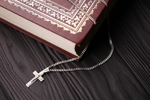 Серебряное ожерелье с крестом-распятием на христианской священной библейской книге на черном деревянном столе Прося благословения у Бога с силой святости, которая приносит удачу