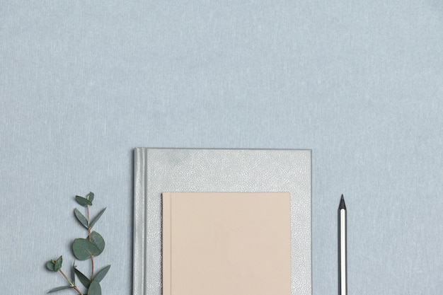 Silver notebook & pencil, pink note, green plant on the grey background