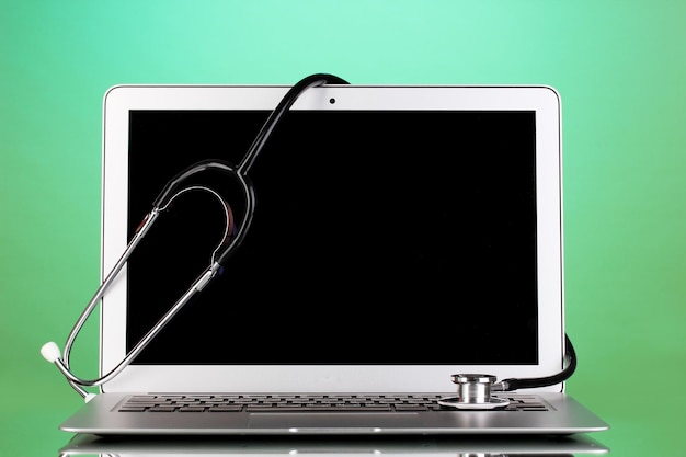 Silver notebook with a stethoscope on green background with reflection