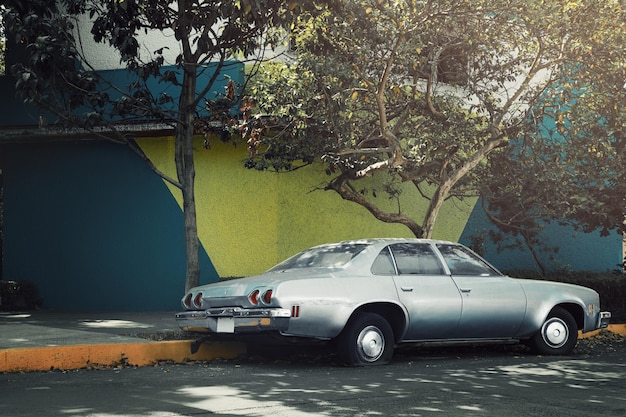 Silver old classic car parked on the side of the street next to painted wall Coyoacan Mexico City