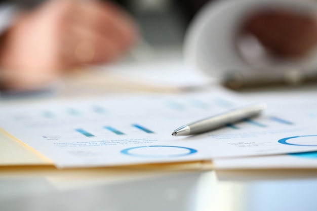 Silver pen lie at important paper on table in office closeup with businessman in background. Paperwork job trade balance bank credit loan money invest payment irs commerce partnership concept